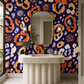 Indigo ocelot leopard print wallpaper in a bathroom with a fluted pedestal sink and gold-framed oval mirror