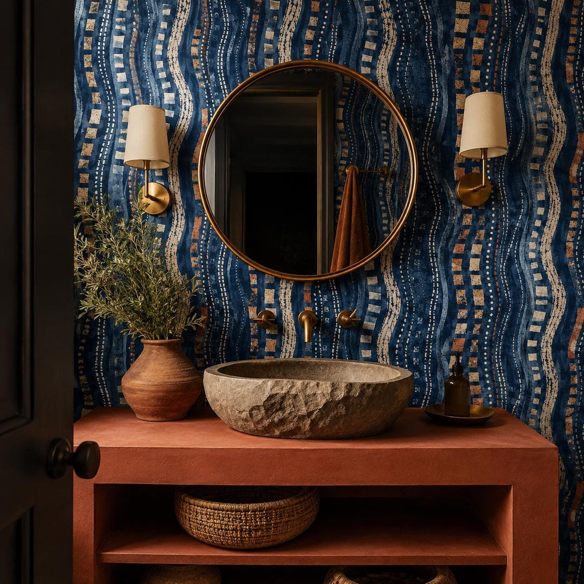 Afrohemian indigo mudcloth wallpaper in a bathroom with a stone vessel sink, round mirror and brass sconces