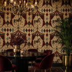Oxblood harlequin circus wallpaper in a dining room with a round black table, red chairs and chandelier