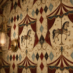 Oxblood harlequin circus wallpaper close-up of carousel horses beside a brass wall sconce