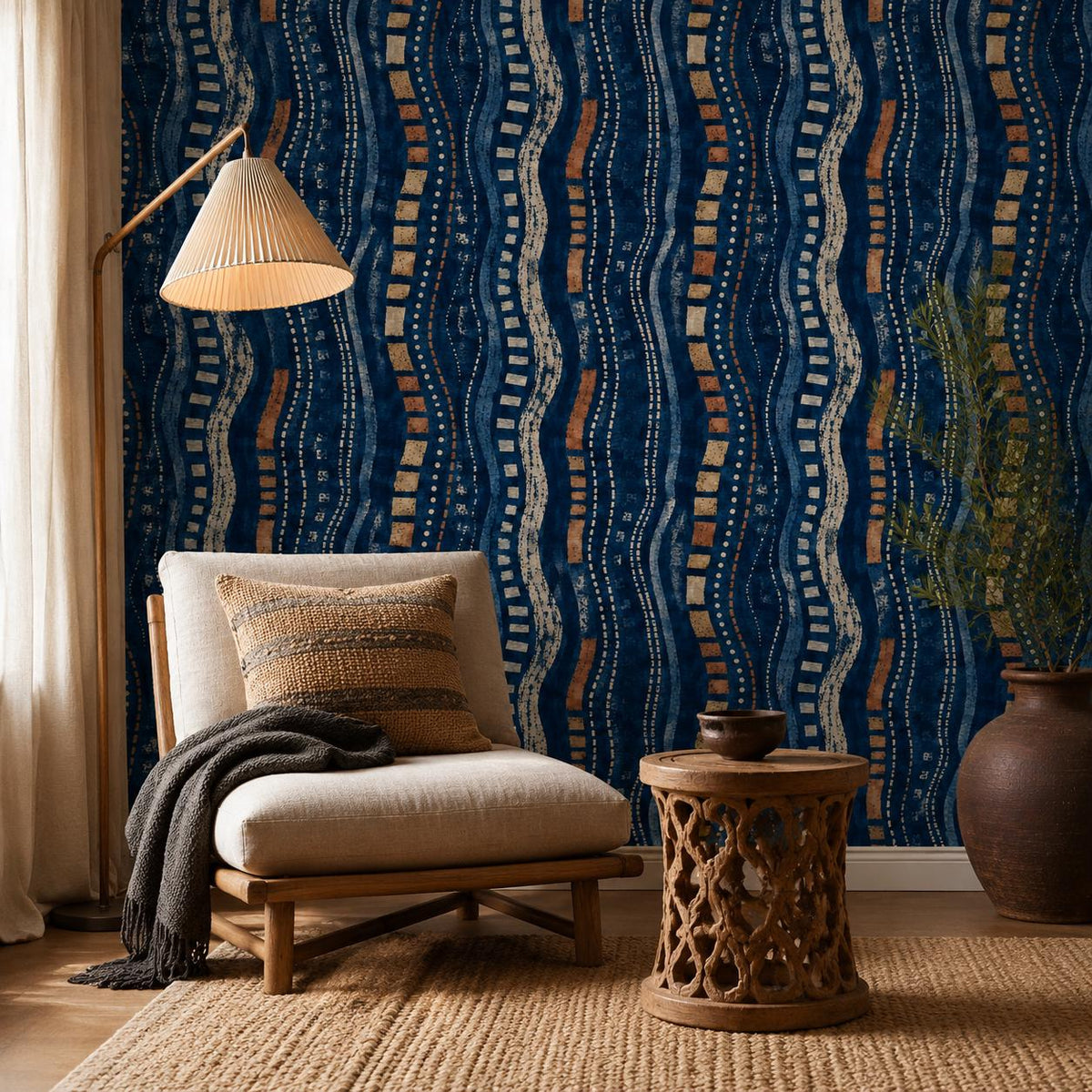 Afrohemian indigo mudcloth wallpaper in a reading corner with a lounge chair, pleated floor lamp and carved side table